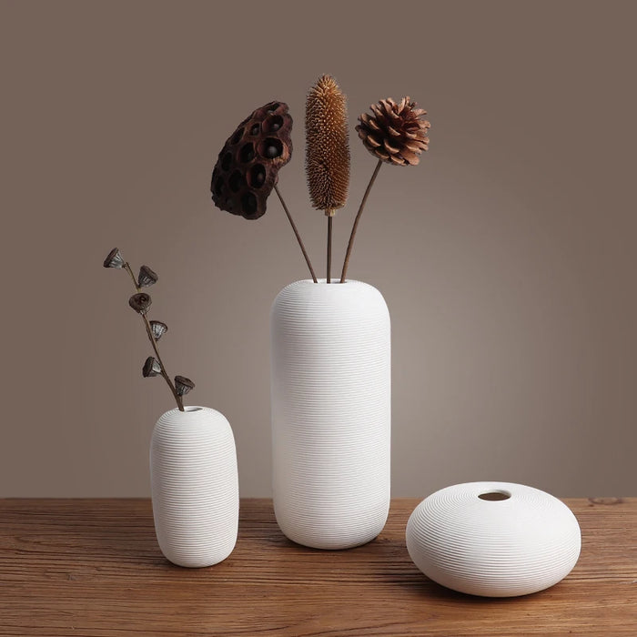 Vase en céramique blanc contemporain avec un bouquet de cônes de pin et de graines de plantes sèches posé sur une table en bois.