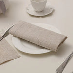 Serviettes de table en lin gris sur une assiette blanche avec une tasse de thé sur le côté.