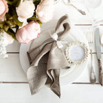 Une élégante table de dîner avec des fleurs de pivoine, une serviette enroulée et un cadre décoratif sur un fond clair.
