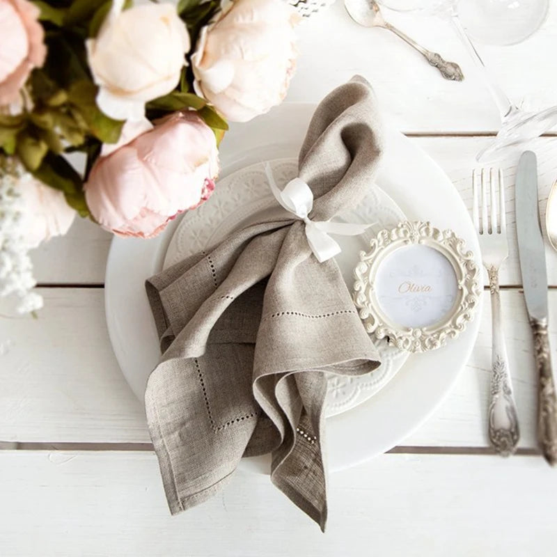 Une élégante table de dîner avec des fleurs de pivoine, une serviette enroulée et un cadre décoratif sur un fond clair.