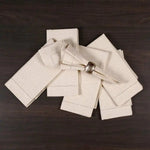 Serviettes blanches pliées avec des coutures décoratives sur un fond en bois sombre.