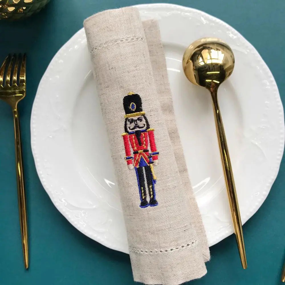 Une serviette de table blanche sur laquelle figure un motif brodé d'un soldat de l'armée britannique, posée sur une assiette blanche avec des couverts dorés.