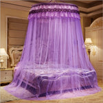 Un lit à baldaquin luxueux et élégant avec des rideaux violets et une couette fleurie, dans une chambre ornée de mobilier ancien et de lampes de table.