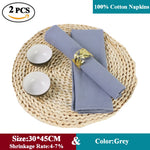 Serviettes de table en coton gris sur un tapis de table en paille tressée, avec deux bols en céramique blanche et un anneau de serviette décoratif.