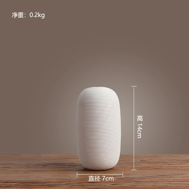 Vase décoratif en céramique blanche de forme cylindrique avec des lignes horizontales proéminentes, sur une table en bois.