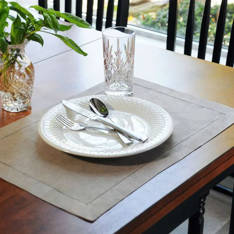 Arrangement élégant de vaisselle sur une table en bois avec un verre en cristal décoratif et une plante verte en arrière-plan, offrant un cadre attrayant pour un repas.