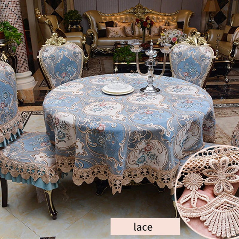La décoration de table luxueuse comprend une nappe ornée de motifs floraux bleus et beiges, ainsi que des éléments décoratifs en dentelle, un chandelier en verre et des fleurs, créant une ambiance élégante et raffinée.