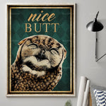 Un gros plan sur le visage d'un oiseau aux plumes dorées et brunes, avec le texte "Nice Butt" en lettrage doré sur un fond vert foncé dans un cadre décoratif.