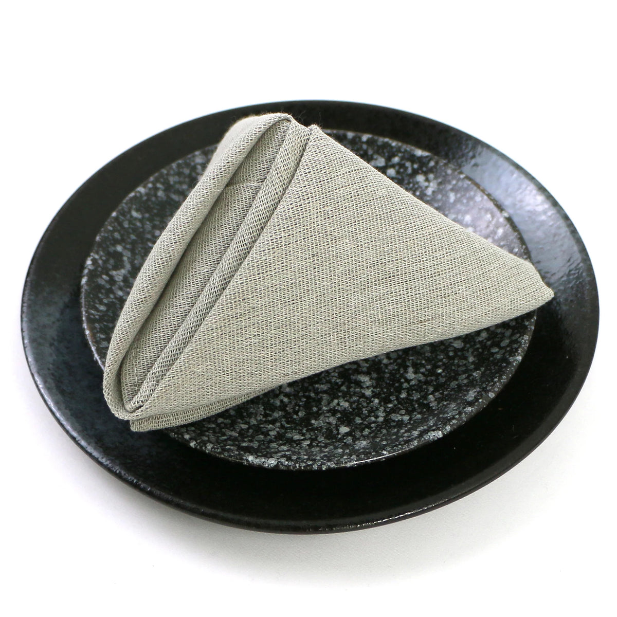 Sur un plat noir et brillant, un linge en lin beige, soigneusement plié en forme de triangle, ajoute une touche d'élégance minimaliste à cette mise en scène.