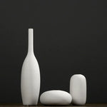Trois vases blancs minimalistes posés sur une surface sombre.