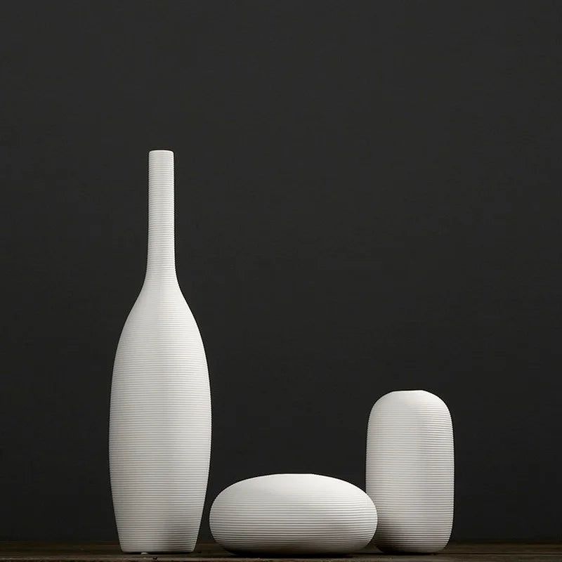 Trois vases blancs minimalistes posés sur une surface sombre.