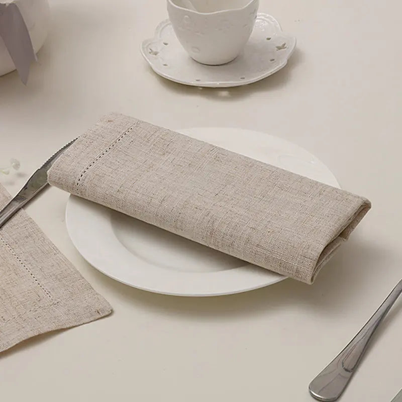 Une serviette en lin grise posée sur une assiette blanche, accompagnée d'une tasse et d'un couteau sur une surface blanche.