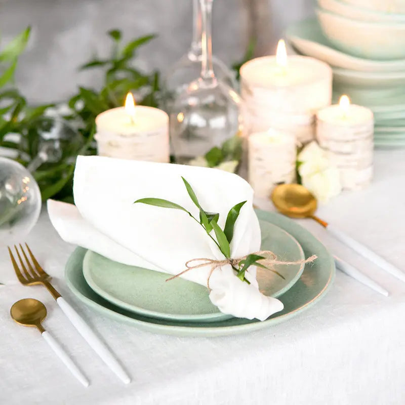 Une table élégamment dressée avec des assiettes vertes, des serviettes blanches, des bougies allumées et des fleurs créant une atmosphère chaleureuse et raffinée.