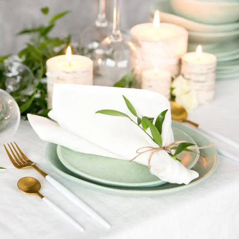 Une belle table de dîner élégamment dressée avec des assiettes vertes, des couverts dorés, des bougies allumées et des fleurs vertes fraîches, créant une ambiance chaleureuse et raffinée.