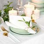 Une belle table de dîner élégamment dressée avec des assiettes vertes, des couverts dorés, des bougies allumées et des fleurs vertes fraîches, créant une ambiance chaleureuse et raffinée.