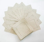 Une pile de serviettes de table beige ornées de bordures brodées, disposées sur une surface blanche.