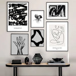Cette galerie murale élégante présente une collection d'œuvres d'art abstraites et minimalistes, notamment des affiches avec des mots, des silhouettes et des formes géométriques noires et blanches, ainsi que des sculptures en verre et en bois sur un meuble en bois.