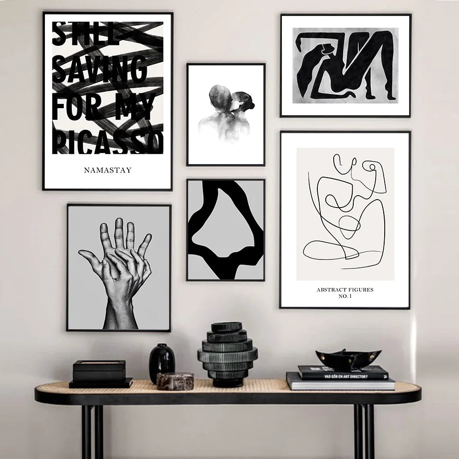 Cette galerie murale élégante présente une collection d'œuvres d'art abstraites et minimalistes, notamment des affiches avec des mots, des silhouettes et des formes géométriques noires et blanches, ainsi que des sculptures en verre et en bois sur un meuble en bois.