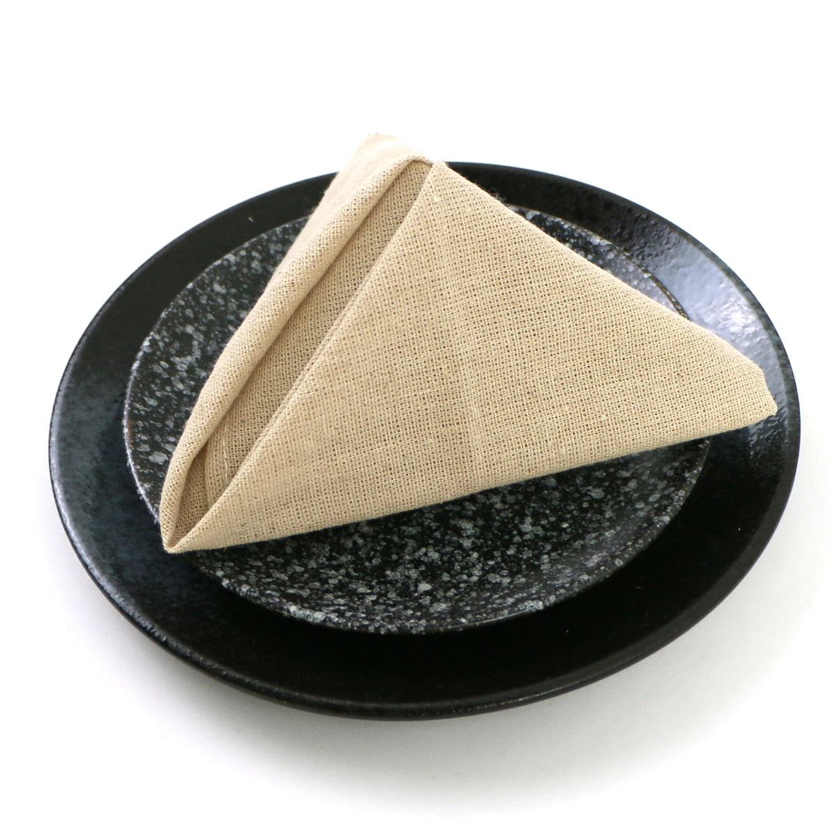 Une serviette de table beige pliée sur une assiette noire avec un motif en relief.
