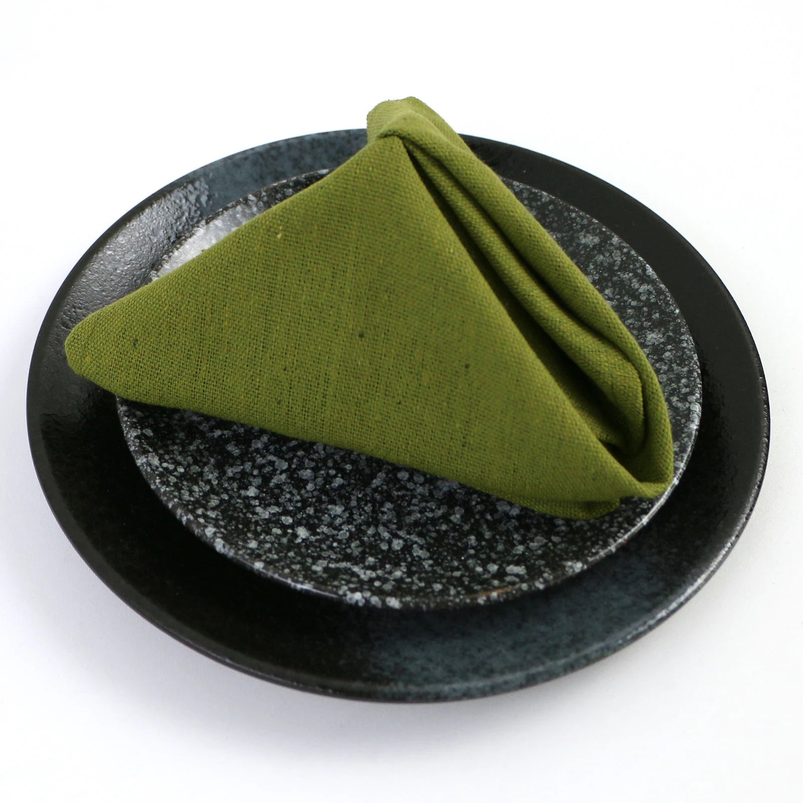 Une serviette de table en lin vert posée sur une assiette noire et grise.