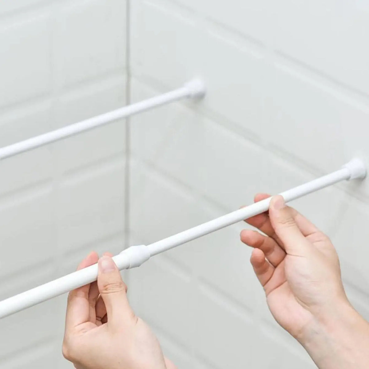 Deux mains installent une tringle blanche sans perçage entre deux parois de douche carrelées.