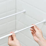 Deux mains installent une tringle blanche sans perçage entre deux parois de douche carrelées.