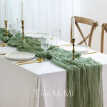 Une table élégante dressée avec des couverts en or, des bougies, des verres de vin et un chemin de table vert pâle, créant une ambiance raffinée et apaisante.