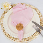Sur un napperon en paille tressée, un serviette en rose et un élégant bouton de rose blanche sont disposés, créant une composition raffinée et harmonieuse.