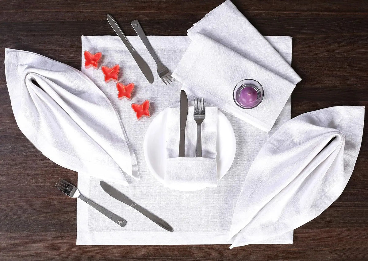Arrangement de couverts élégant avec des serviettes de table blanches, des ustensiles argentés et de petites formes rouges en forme d'étoile sur un fond sombre en bois.