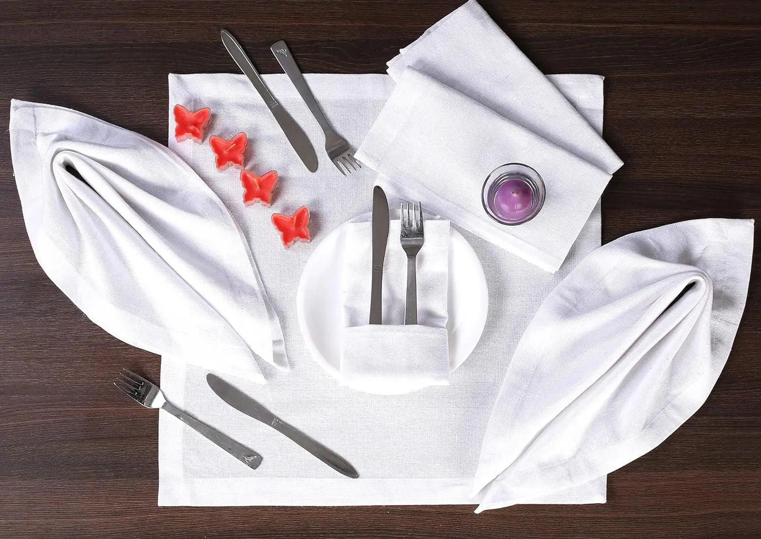 Arrangement de couverts élégant avec des serviettes de table blanches, des ustensiles argentés et de petites formes rouges en forme d'étoile sur un fond sombre en bois.