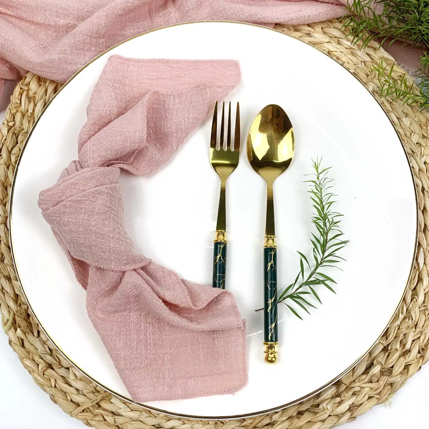 Une belle table de repas avec des serviettes roses en lin, des couverts en or et une verdure fraîche qui apportent une touche de naturel.