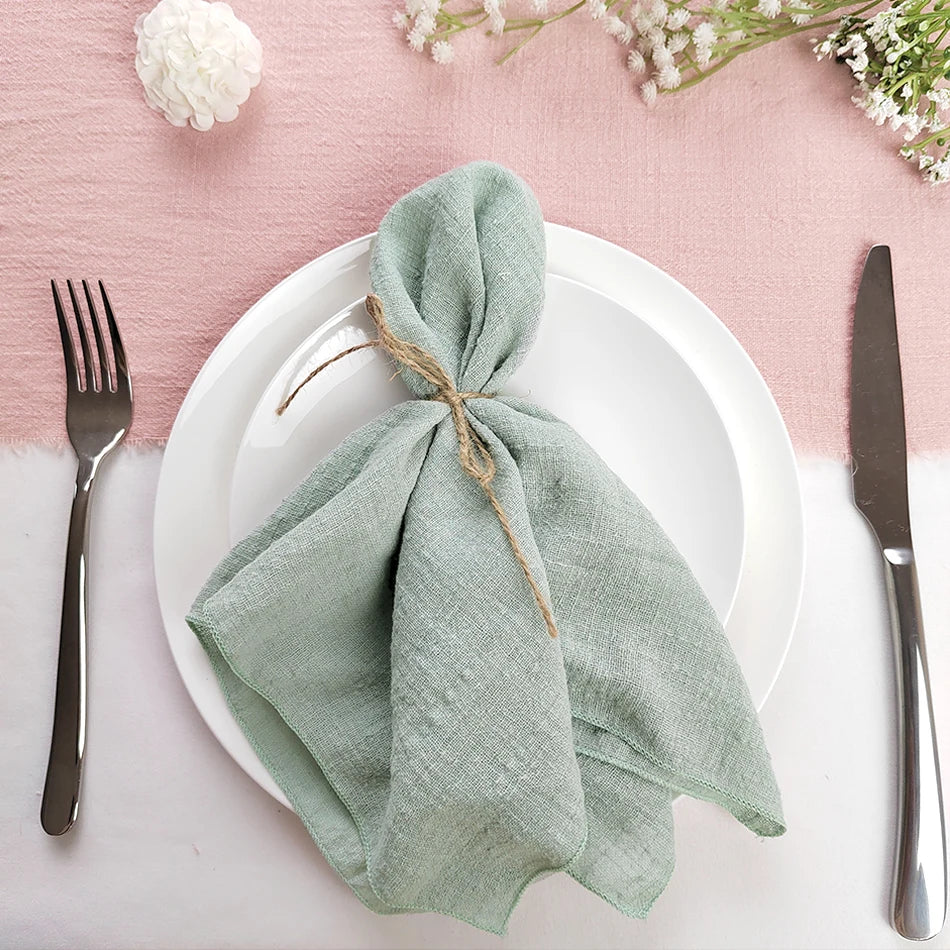 Arrangement élégant de table avec une serviette nouée délicatement sur une assiette blanche, entouré de fleurs fraîches sur un fond rose pastel.