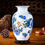 Un vase en porcelaine blanche décoré de motifs de dragons bleus et jaunes, avec une base en bois sombre.