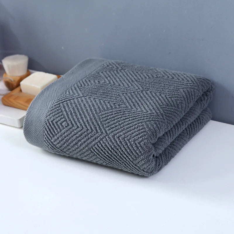 Une couverture grise aux motifs texturés, posée sur une surface blanche à côté de quelques accessoires.