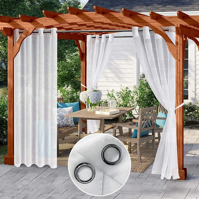 Rideaux extérieurs imperméables blancs suspendus à une pergola en bois, encadrant un salon de jardin élégant avec table et chaises, dans un cadre verdoyant.