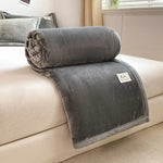 Une couverture gris foncé en velours douillet et confortable, parfaite pour se blottir et se réchauffer sur un canapé.