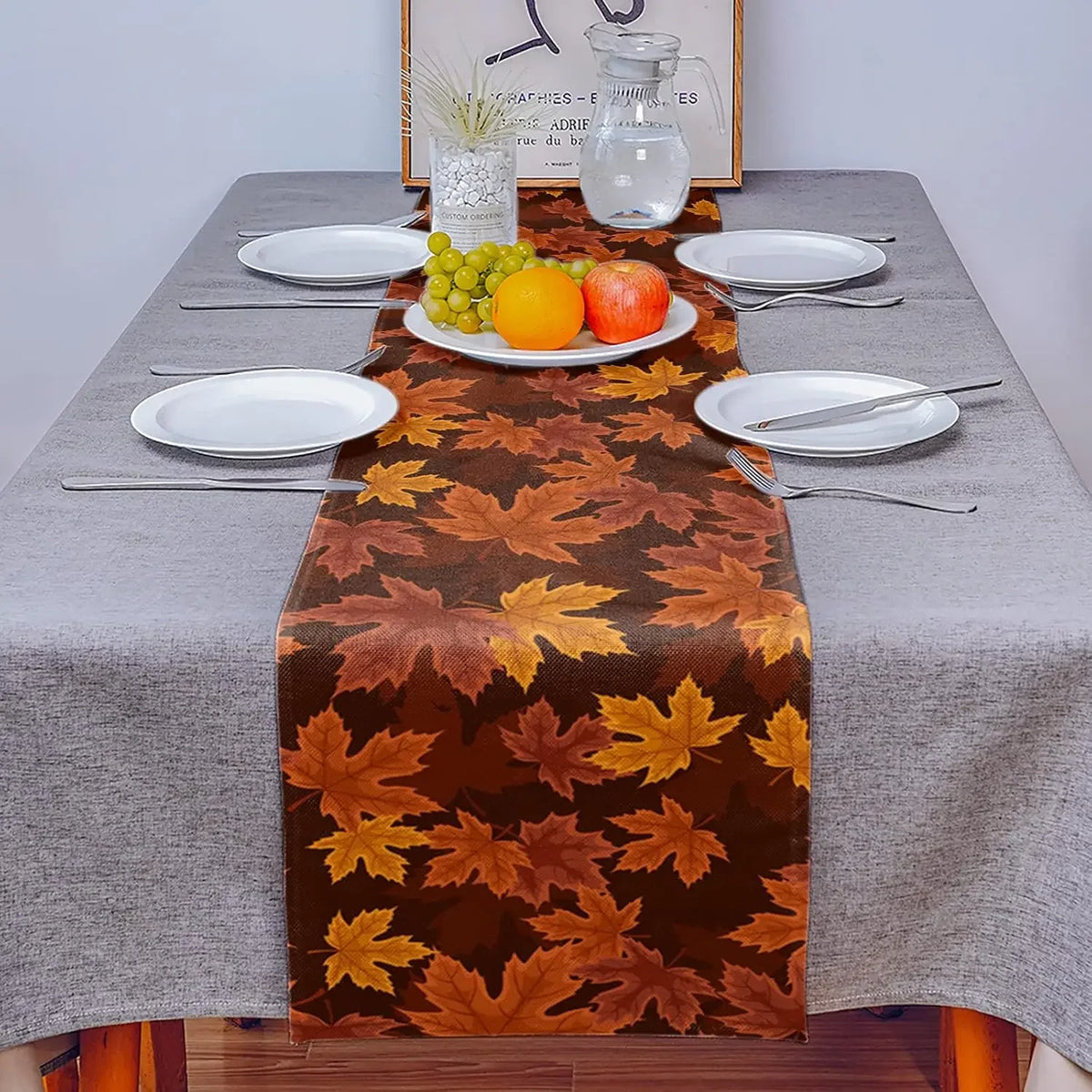 Une table de salle à manger avec des assiettes, des couverts et un centre de table décoré de feuilles d'automne en couleurs chaudes.