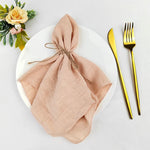 Une belle nappe de table beige, élégamment pliée, posée sur une assiette blanche avec des couverts dorés et une décoration florale.