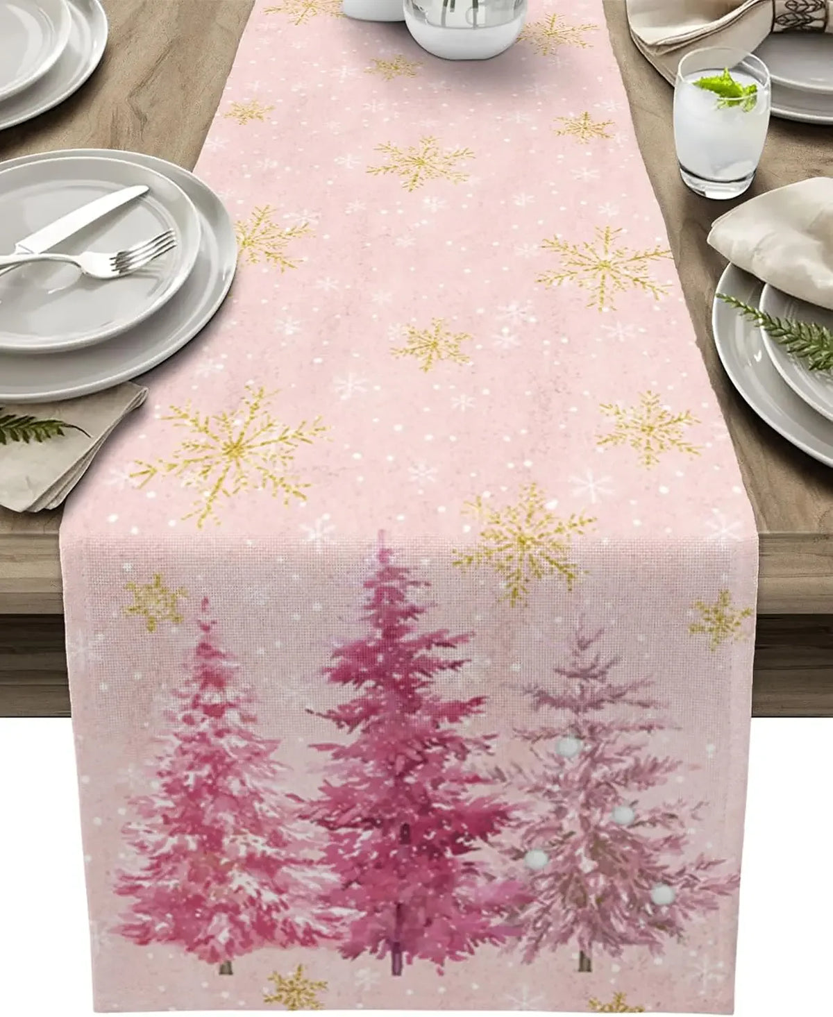 Chemin de table rose décoré de motifs de flocons de neige dorés et d'arbres de Noël roses sur un fond clair.