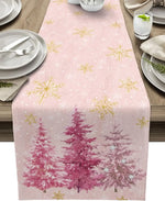 Chemin de table rose décoré de motifs de flocons de neige dorés et d'arbres de Noël roses sur un fond clair.