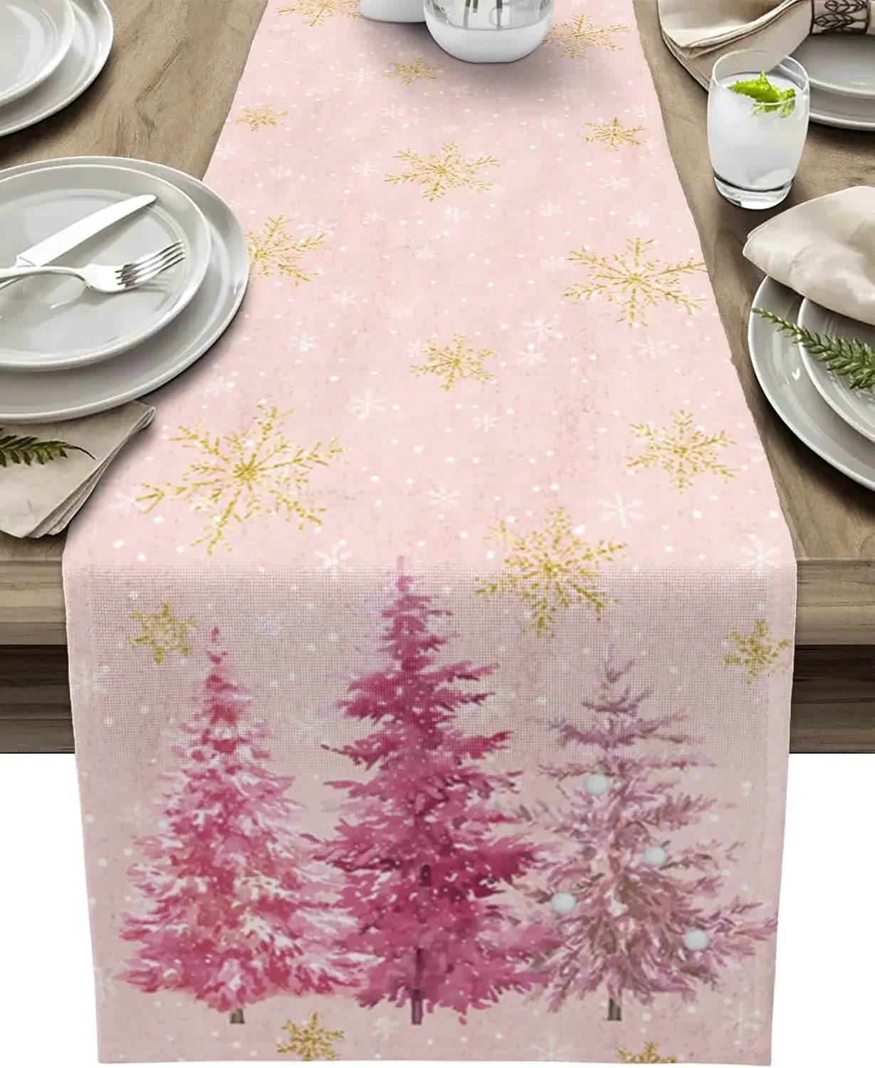 Chemin de table rose décoré de motifs de flocons de neige dorés et d'arbres de Noël roses sur un fond clair.