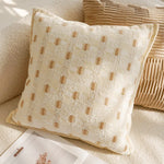 Coussin décoratif beige pâle avec des motifs de pois dorés disposés de manière régulière, placé sur un canapé dans un intérieur élégant et apaisant.
