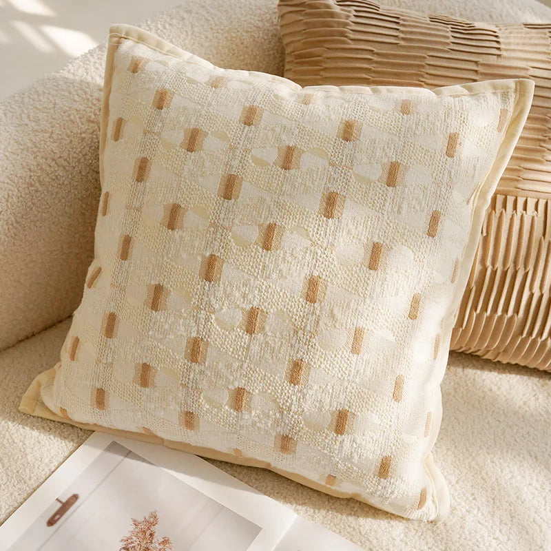 Coussin décoratif beige pâle avec des motifs de pois dorés disposés de manière régulière, placé sur un canapé dans un intérieur élégant et apaisant.