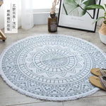 Tapis rond décoratif à motifs géométriques ethniques gris et blanc, posé au sol dans un intérieur moderne avec des plantes vertes.