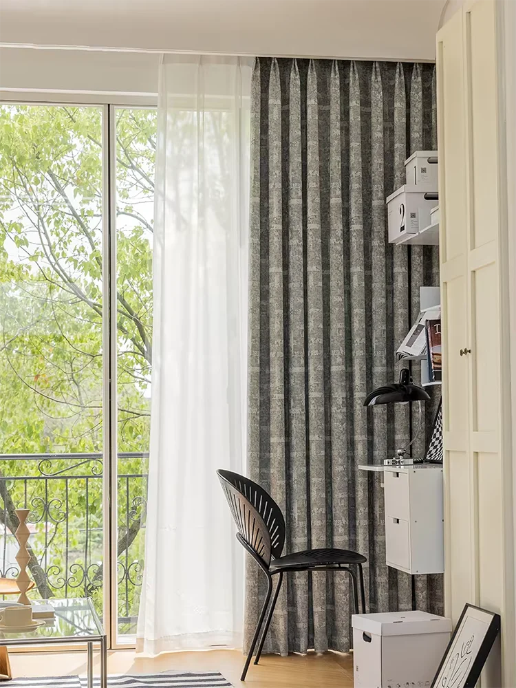 Rideau moderne gris foncé et voilage blanc pour salon contemporain, idéal pour maximiser la lumière naturelle tout en préservant l'intimité. Ambiance élégante avec vue sur l'extérieur verdoyant. Parfait pour une décoration intérieure sophistiquée.