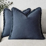 Coussin gris foncé orné de franges, créant une atmosphère cocooning et confortable dans un intérieur.