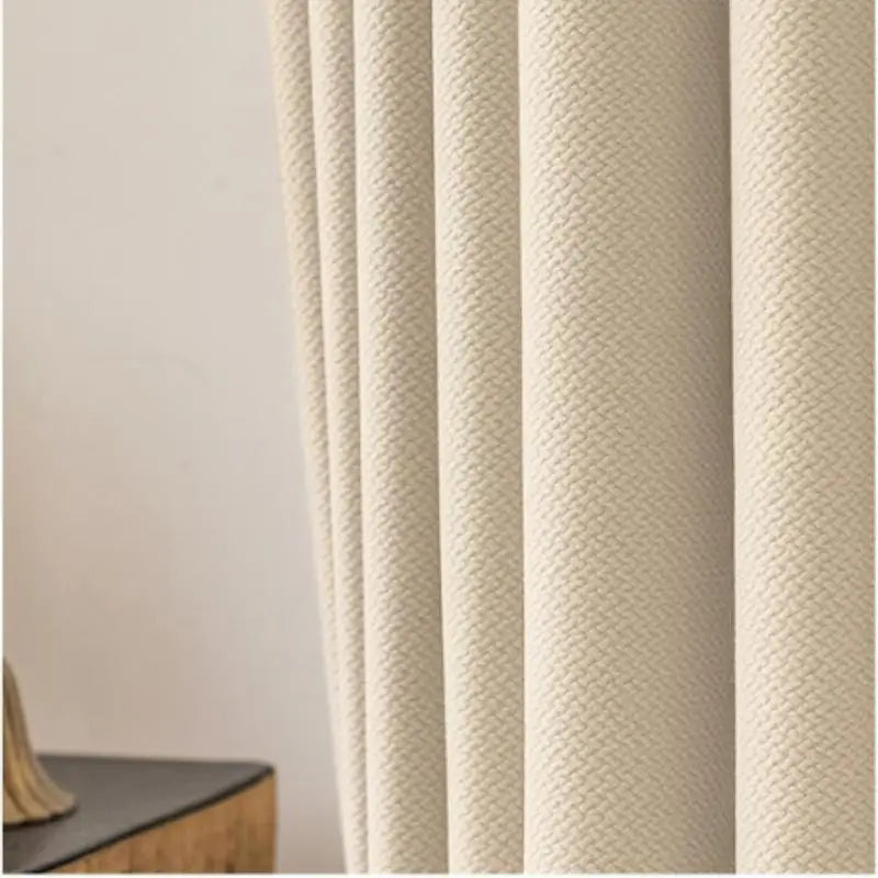 Gros plan sur la texture tissée d’un rideau beige clair, mettant en valeur son tombé fluide et son tissu épais.