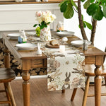 Une élégante table dressée avec un bouquet de fleurs, des figurines de lapins, des plats et un chemin de table décoré de motifs printaniers.