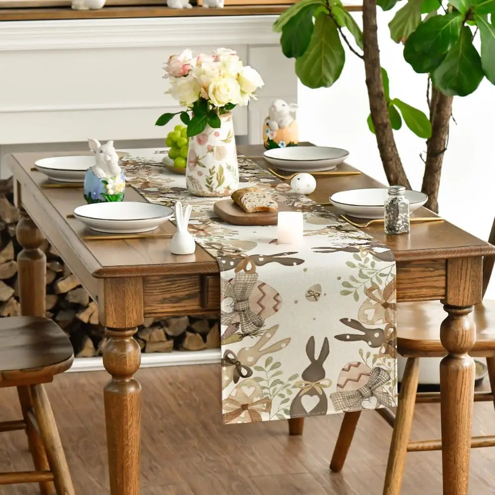 Une élégante table dressée avec un bouquet de fleurs, des figurines de lapins, des plats et un chemin de table décoré de motifs printaniers.