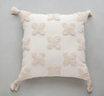 Coussin décoratif blanc en forme de fleurs avec pompons aux coins.